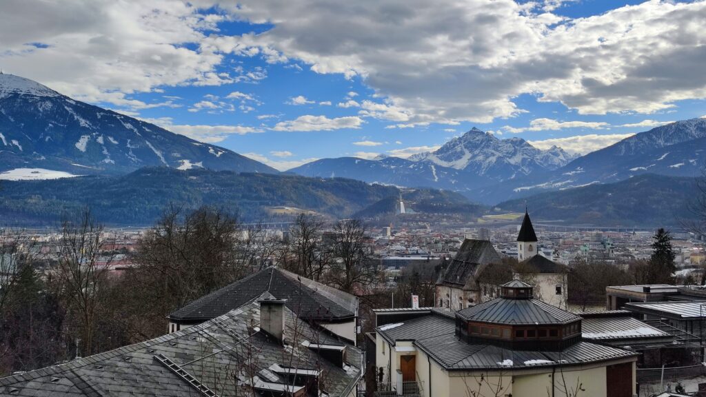 Panoramablick auf Tirol im Frühling mit schneebedeckten Bergen und historischen Gebäuden.